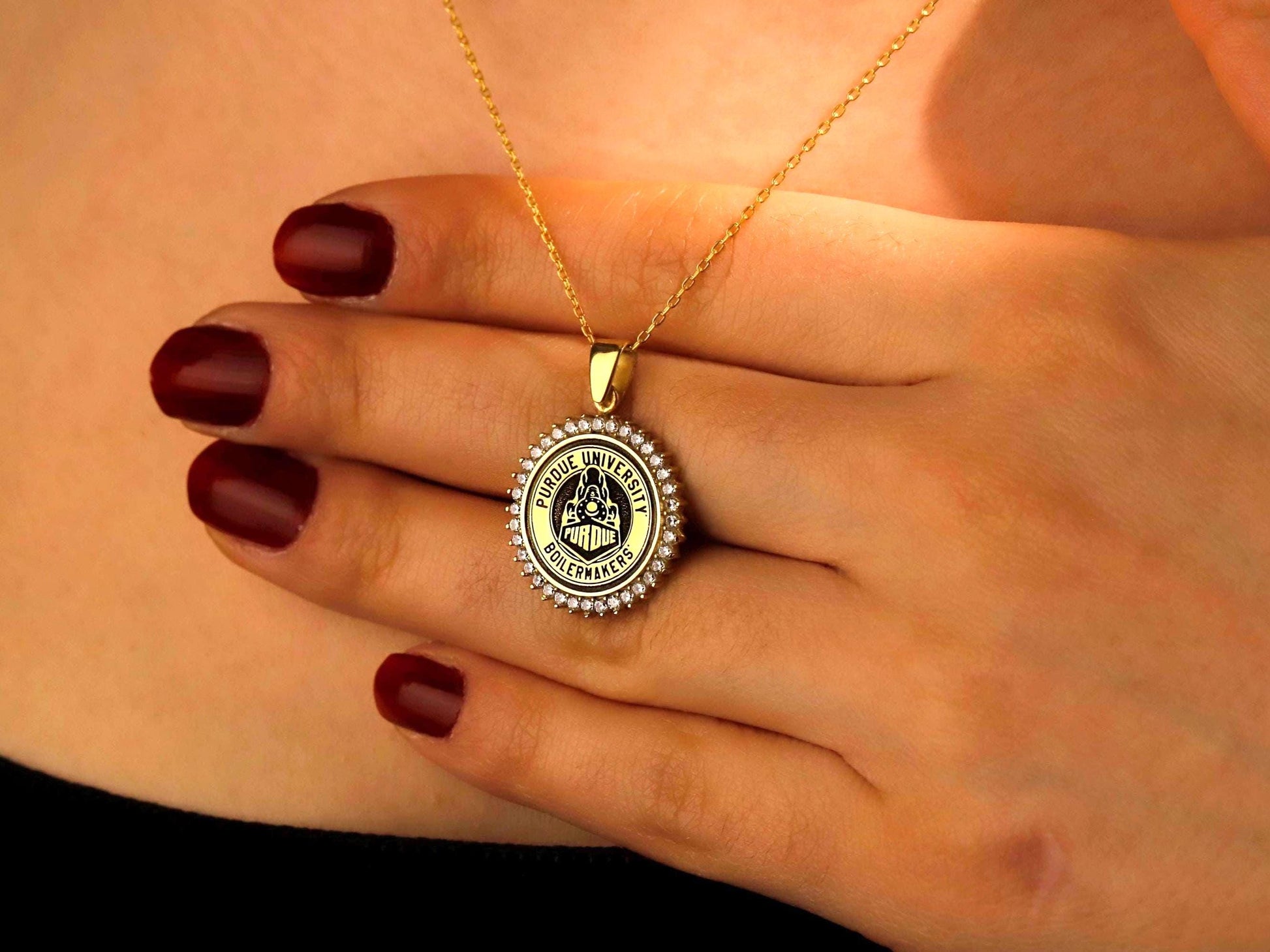 Gold necklace with a round pendant held by a hand with red nail polish.
