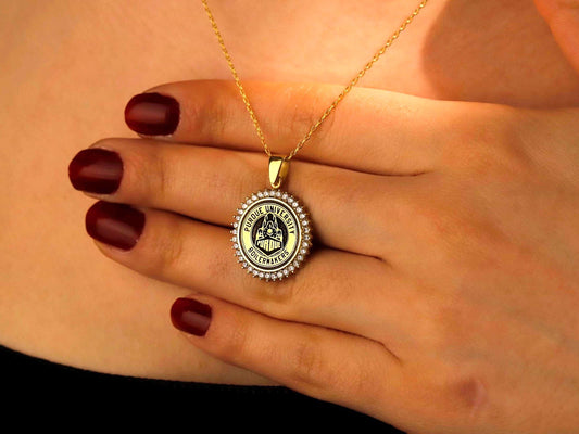 Gold necklace with a round pendant held by a hand with red nail polish.