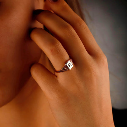 Hand with a ring featuring a letter 'R' on a blurred background