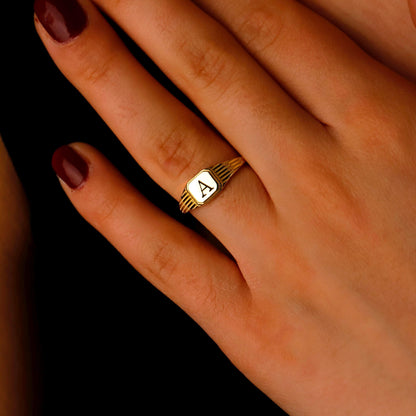 Gold ring with letter 'A' on a hand against a dark background