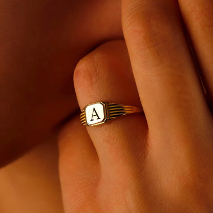 Gold ring with a letter 'A' on a person's finger against a warm-toned background