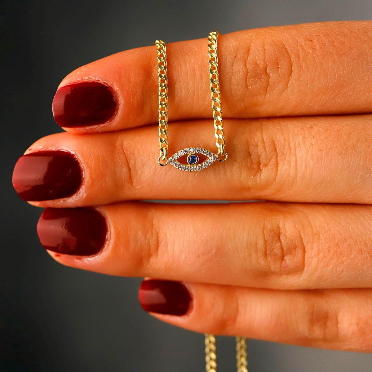 Gold necklace with an eye-shaped pendant held between fingers with red nail polish.