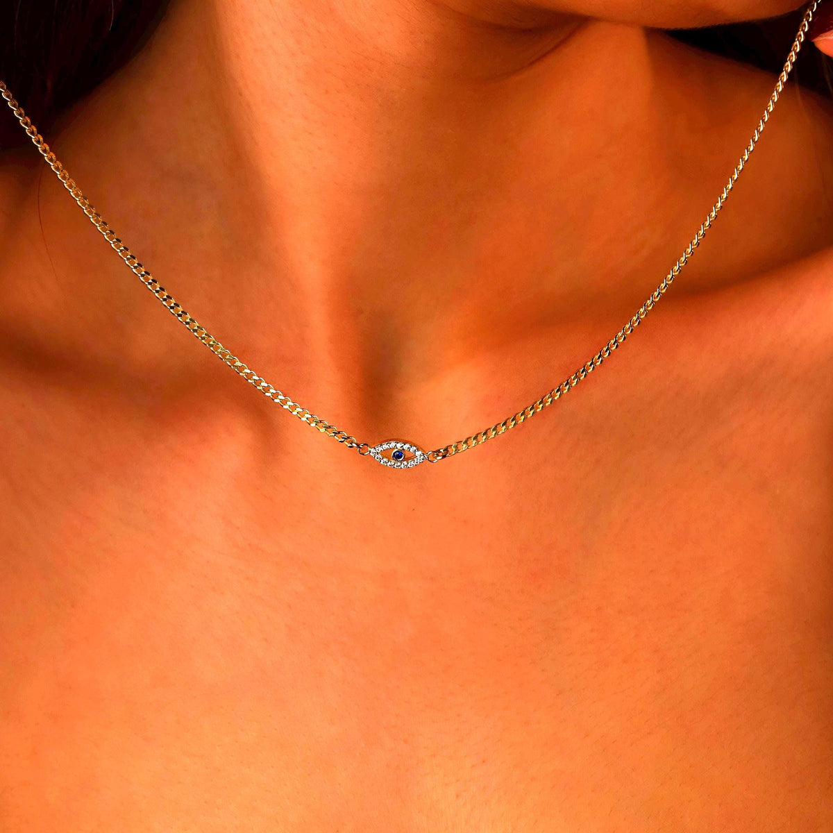 Gold necklace with a blue gemstone on a person's neck against an orange background