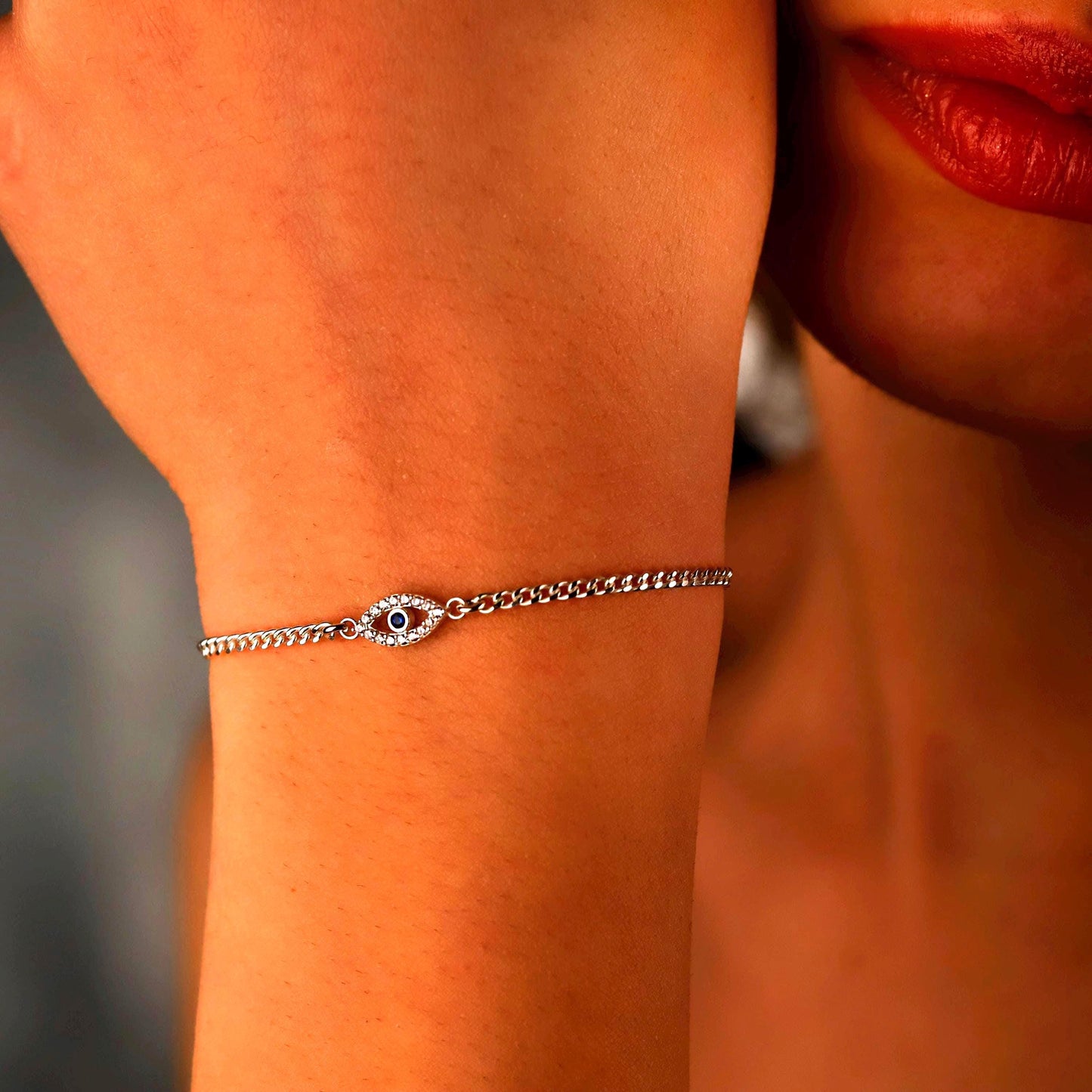Silver bracelet with an eye design on a person's wrist, with a blurred background.