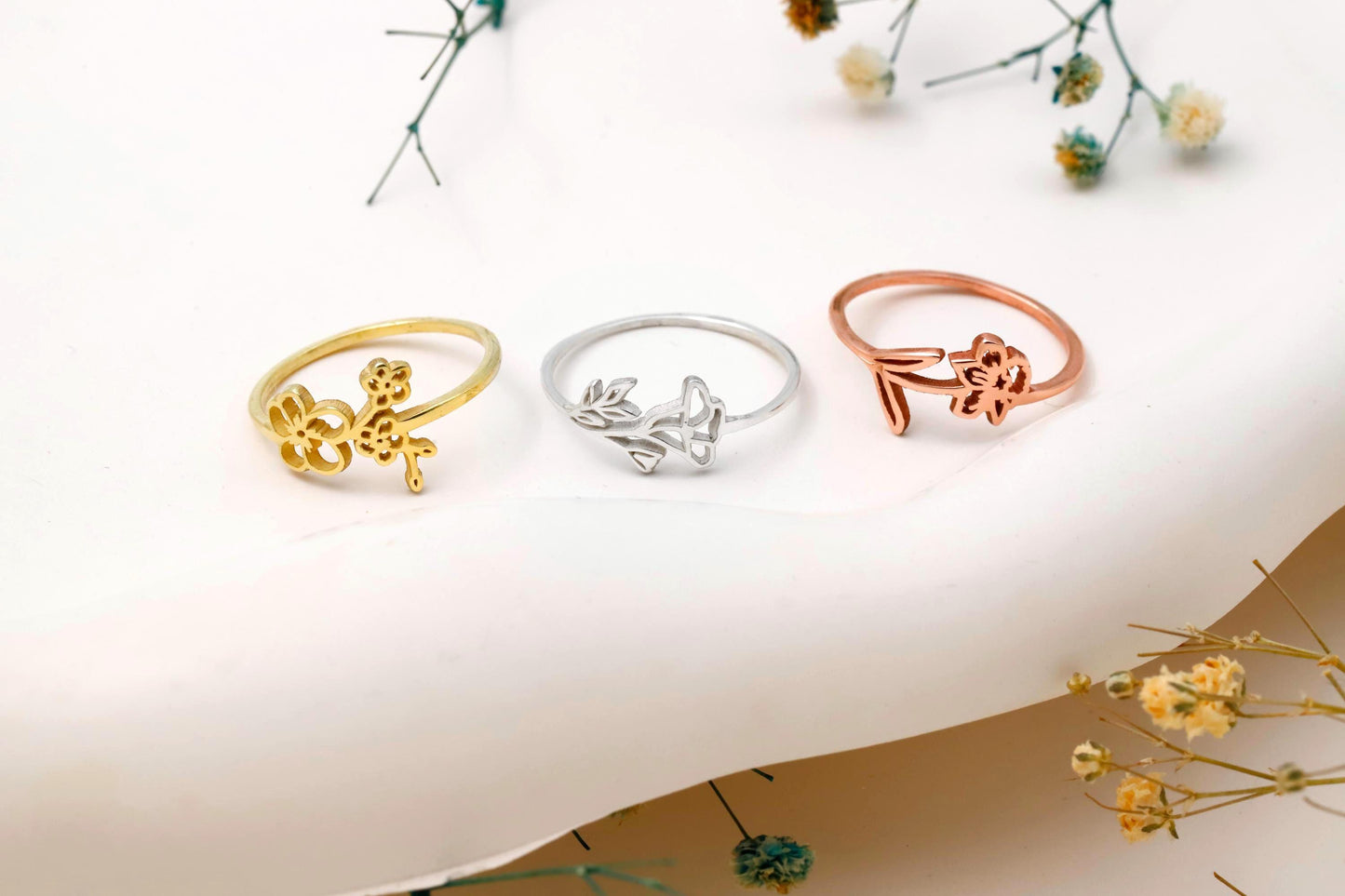 Three rings in gold, silver, and rose gold on a white background with floral elements.