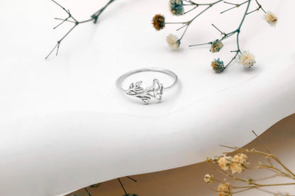 Silver ring with floral design on a white surface with dried flowers.