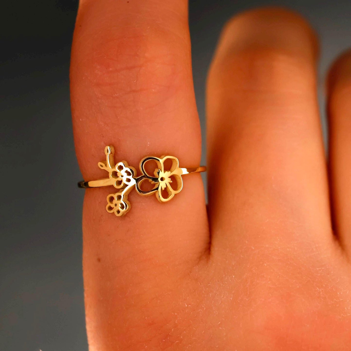 Gold ring with floral design on a finger against a dark background