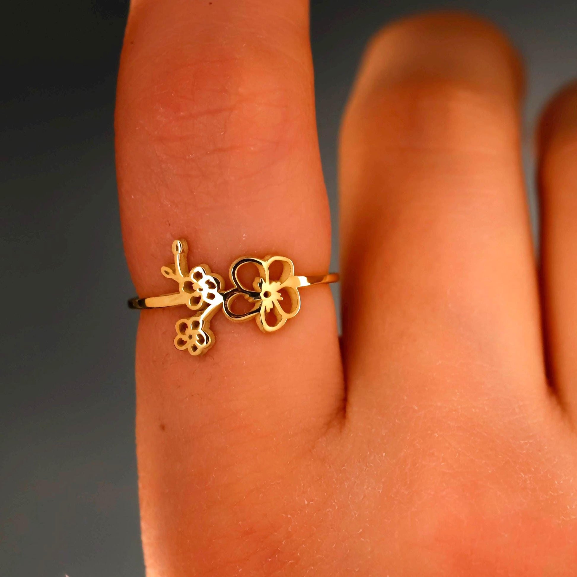 Gold ring with floral design on a finger against a dark background