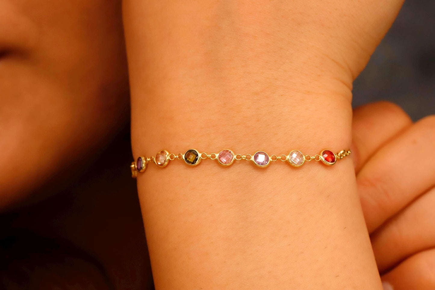 Gold bracelet with colorful beads on a wrist against a neutral background