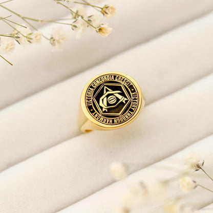 Gold ring with engraved design on a light fabric background with small flowers.