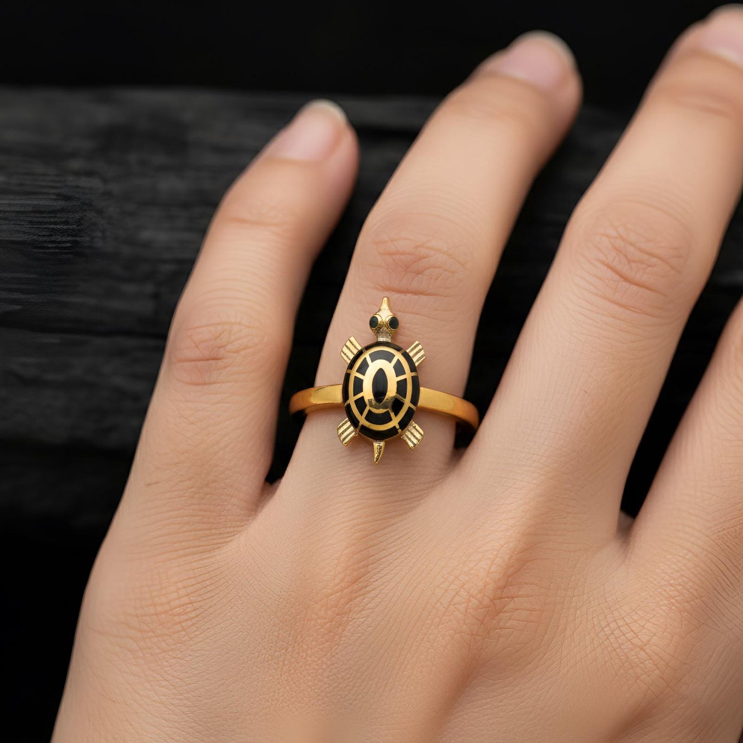 Gold ring with a black turtle design on a hand against a dark background