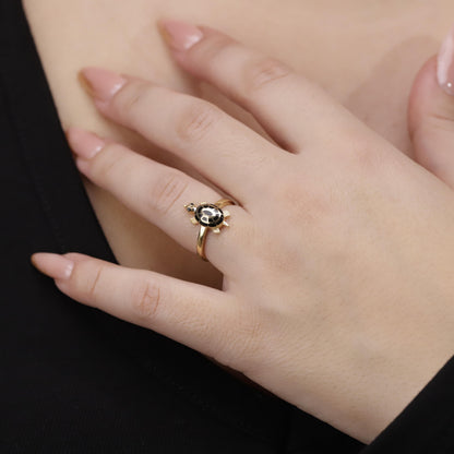 Close-up of a hand wearing a gold ring with a black gemstone on a dark background