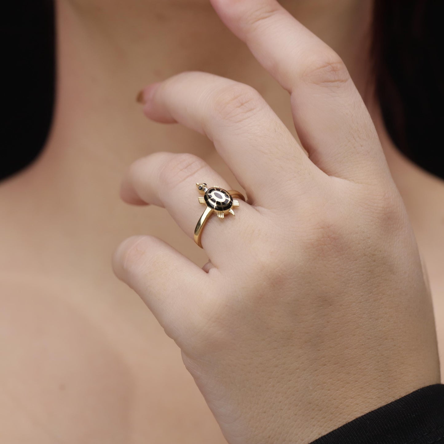 Gold ring with a black stone on a person's finger against a neutral background