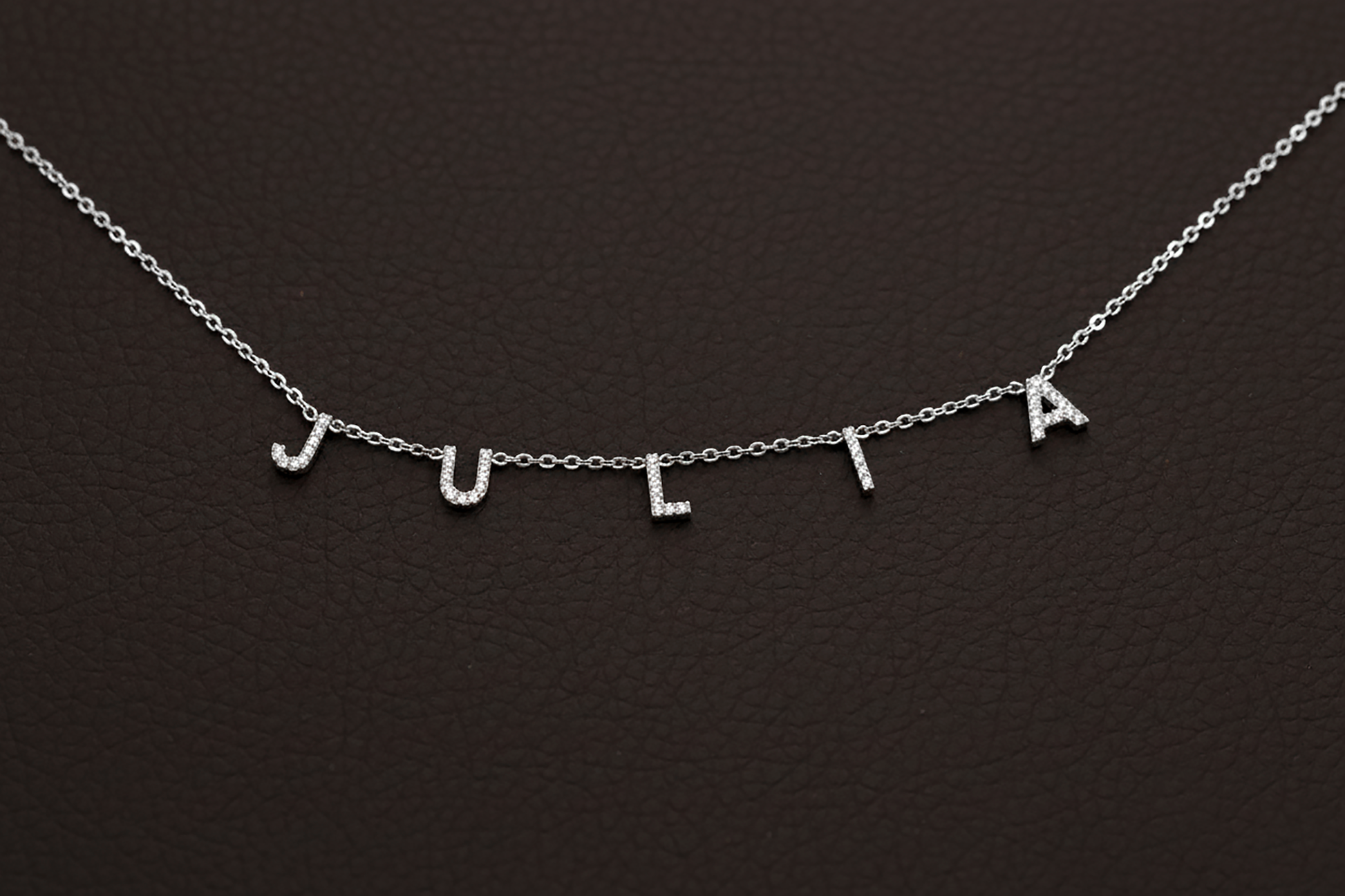Silver necklace with 'JULIA' letters on a dark background