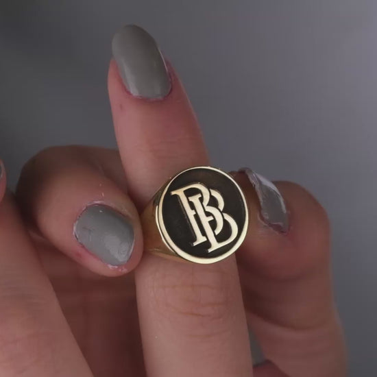 A close-up image of a woman's hand wearing a silver ring with intertwined initials.