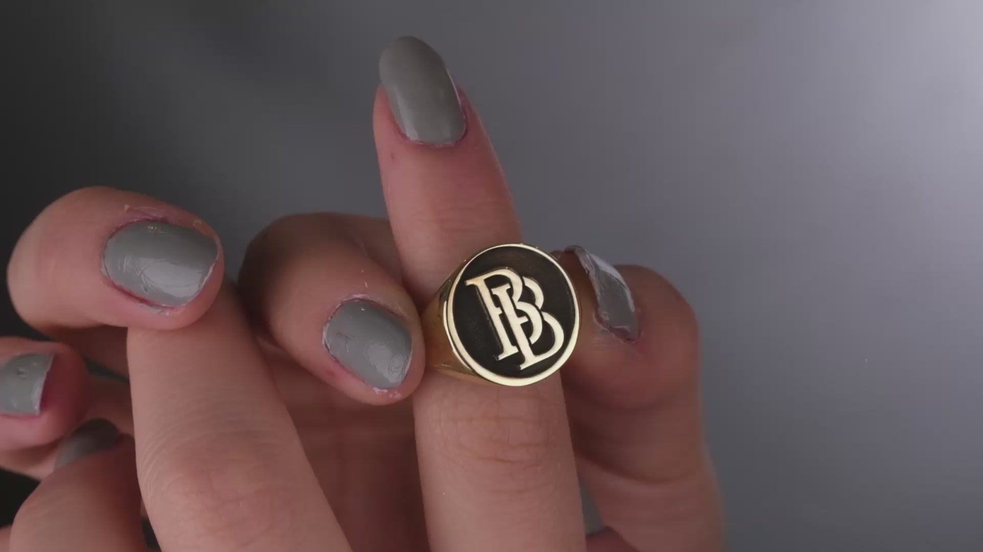A close-up image of a woman's hand wearing a silver ring with intertwined initials.