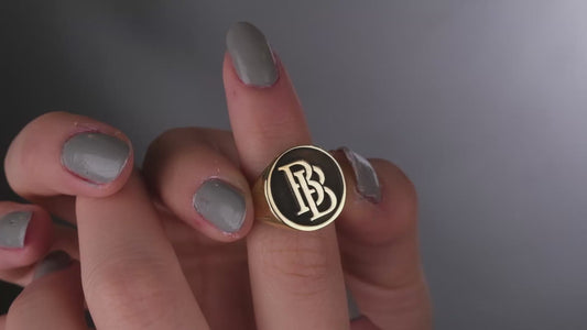 A close-up image of a woman's hand wearing a silver ring with intertwined initials.