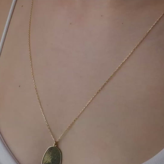 Hand holding five gold necklaces with different pendants against a blurred background