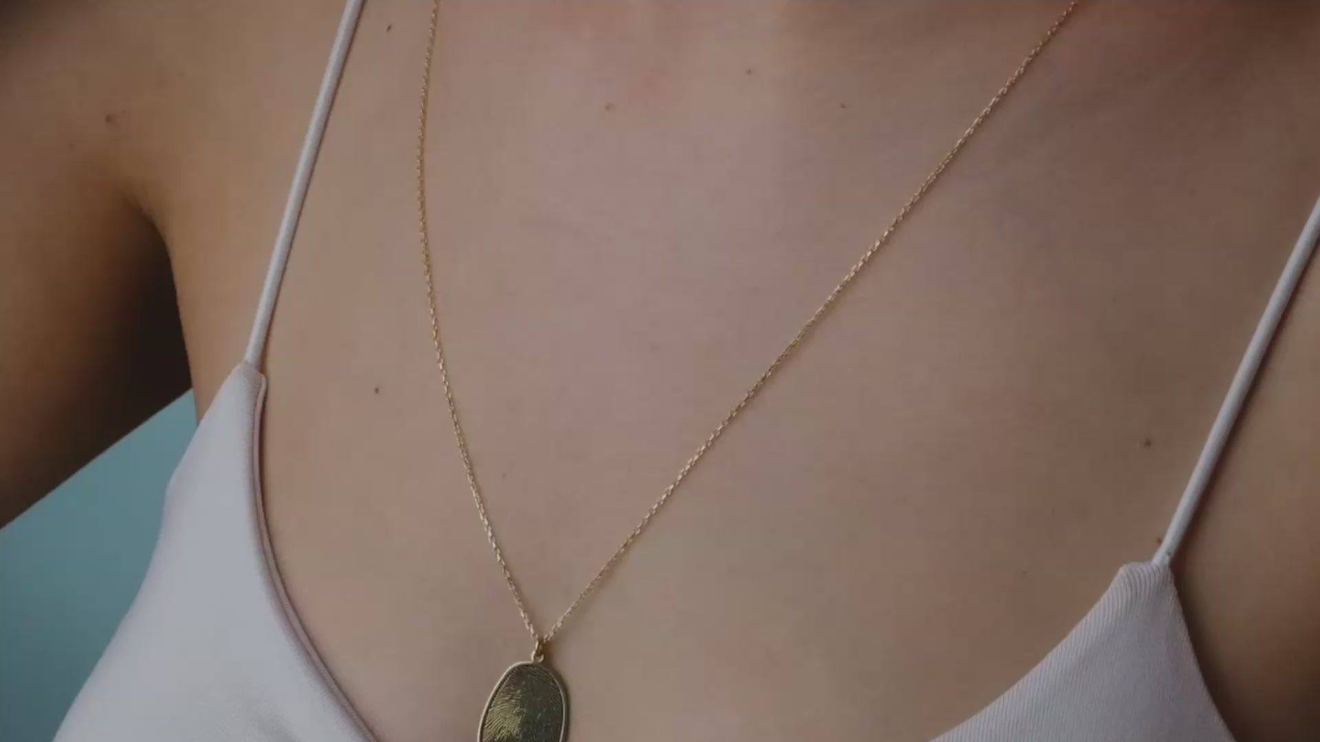 Hand holding five gold necklaces with different pendants against a blurred background