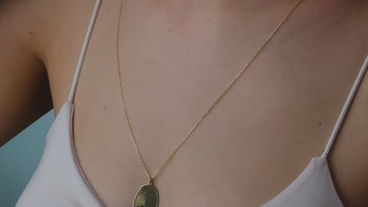 Hand holding five gold necklaces with different pendants against a blurred background