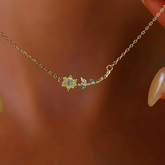 Gold necklace with floral design worn by a person against a blurred background
