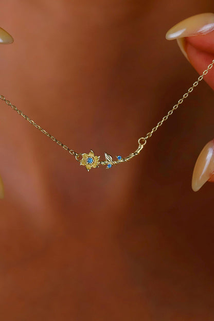 Gold necklace with floral design worn by a person against a blurred background