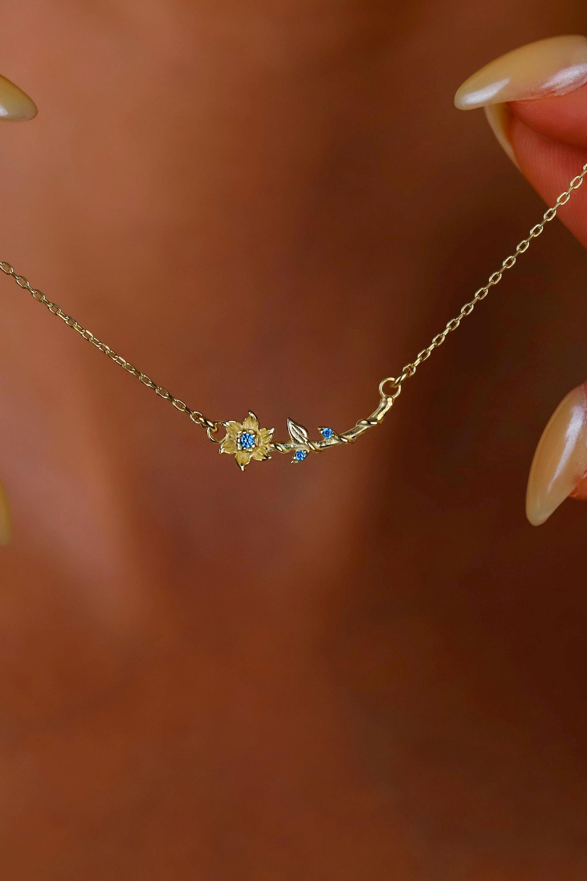 Gold necklace with floral design worn by a person against a blurred background