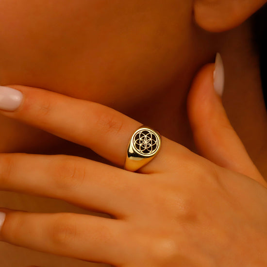 A gold signet ring featuring a geometric "Seed of Life" engraving, shown being worn on a hand and showcased from various angles. A product by SilverGoldandRose.com.