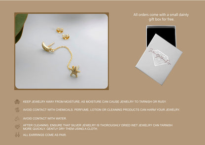 Gold earrings on a reflective surface with a small gift box and care instructions.
